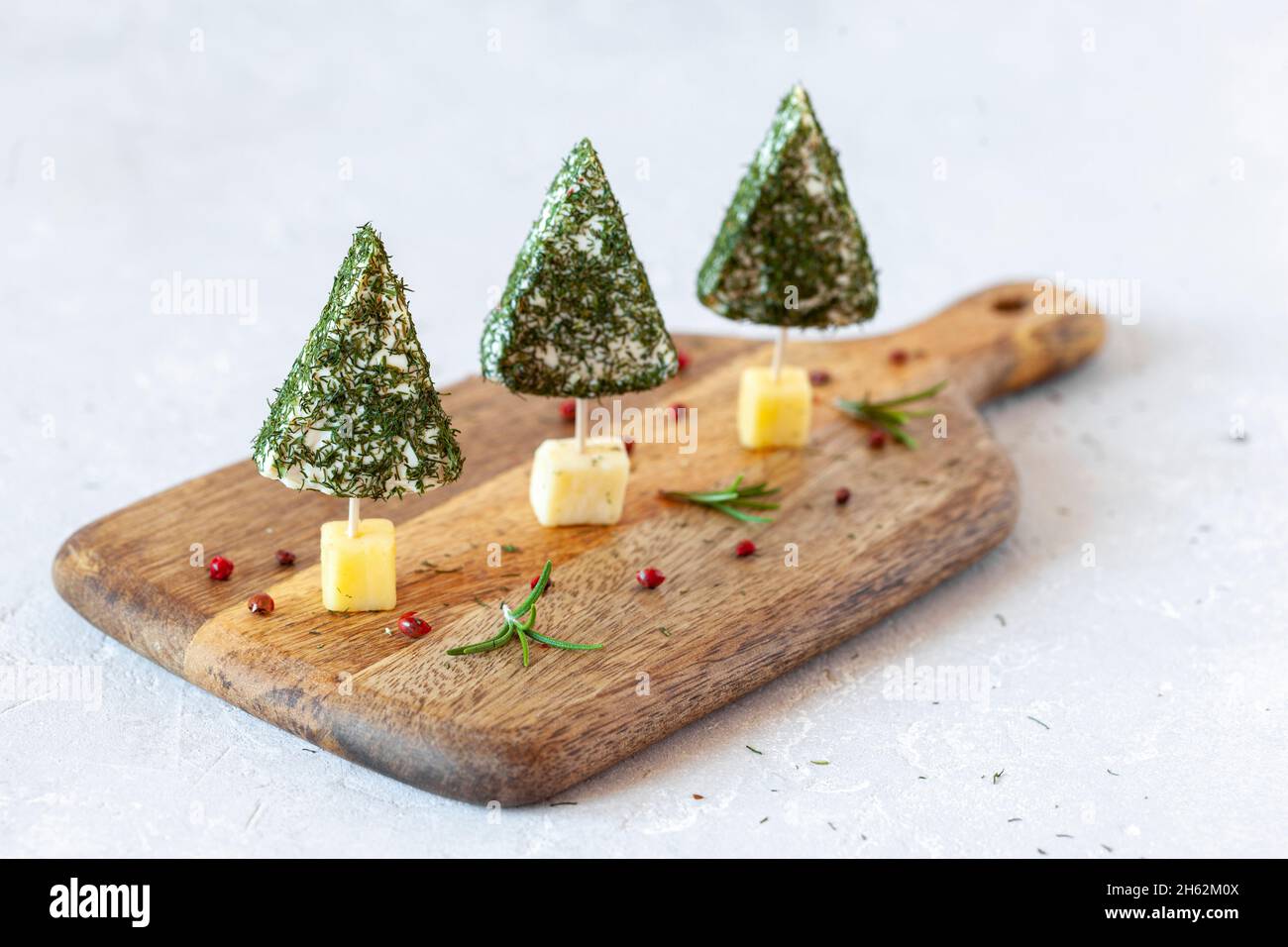 Christmas trees appetizers made of soft cheese on a cutting board on white background, closeup, side view Stock Photo