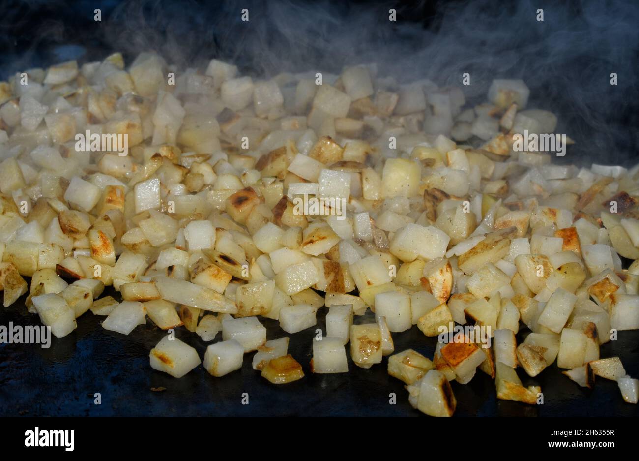 Hash browns being cooked on a griddle, with steam rising from the small cubed potatoes Stock Photo