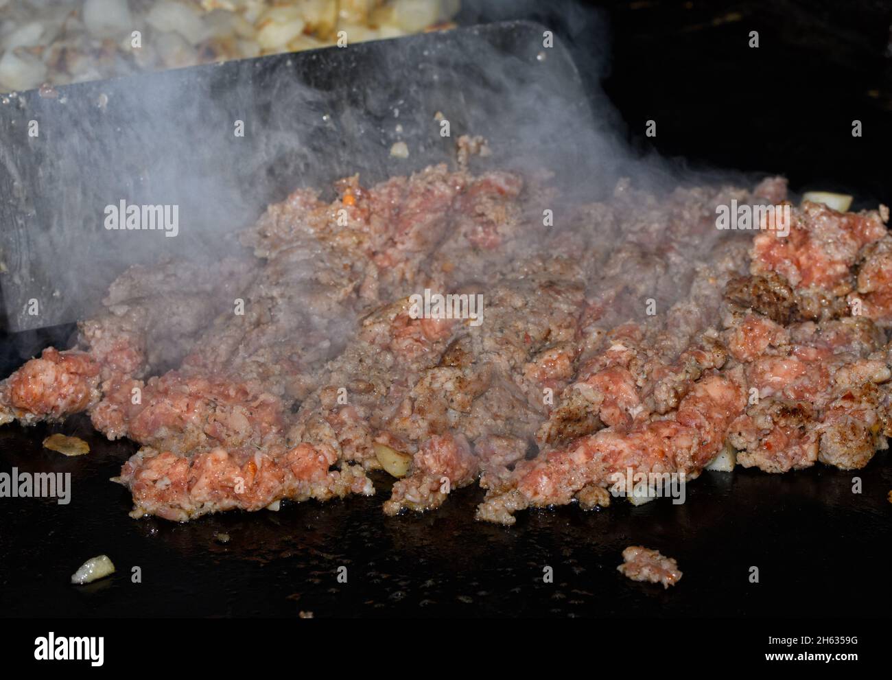Ground sausage being cooked on griddle in preparation for breakfast casserole; with heavy steam rising, and a metal spatula on the background moving t Stock Photo