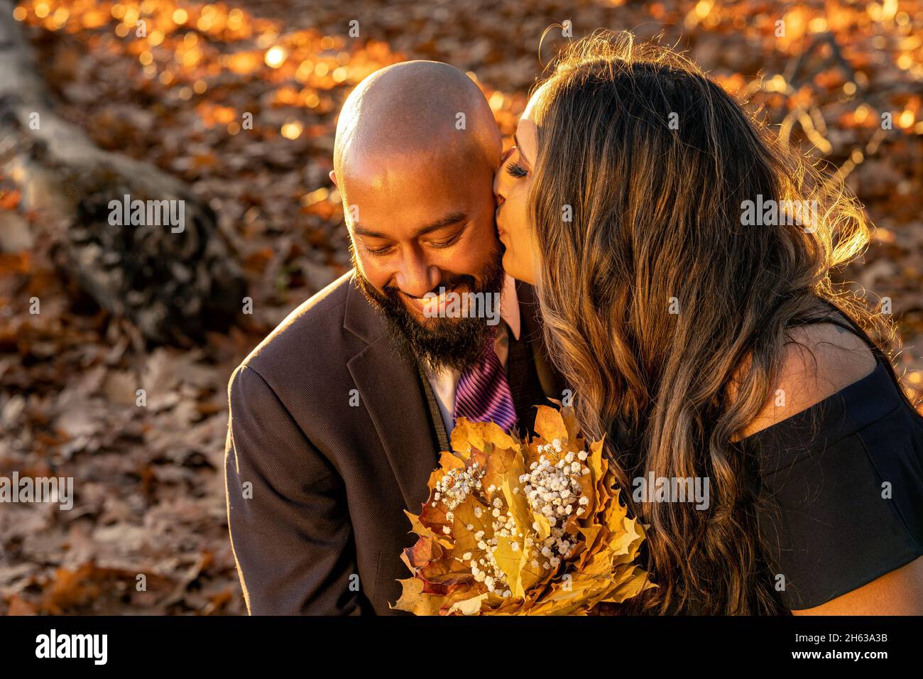 Emotional, full of love photo of a well dressed mixed race couple hugging and holding kissing each other at sunset in a city park in Vancouver, Britis Stock Photo
