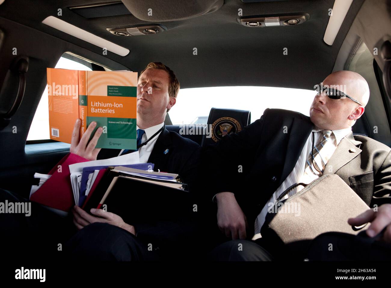 White House Trip Director Marvin Nicholson, left, reads a book on lithium-ion batteries, while riding in the support vehicle from Joint Base Andrews, Maryland, en route to the White House, April 2, 2010. Jeffrey Kueter, a White House physician, is seated at right. Stock Photo