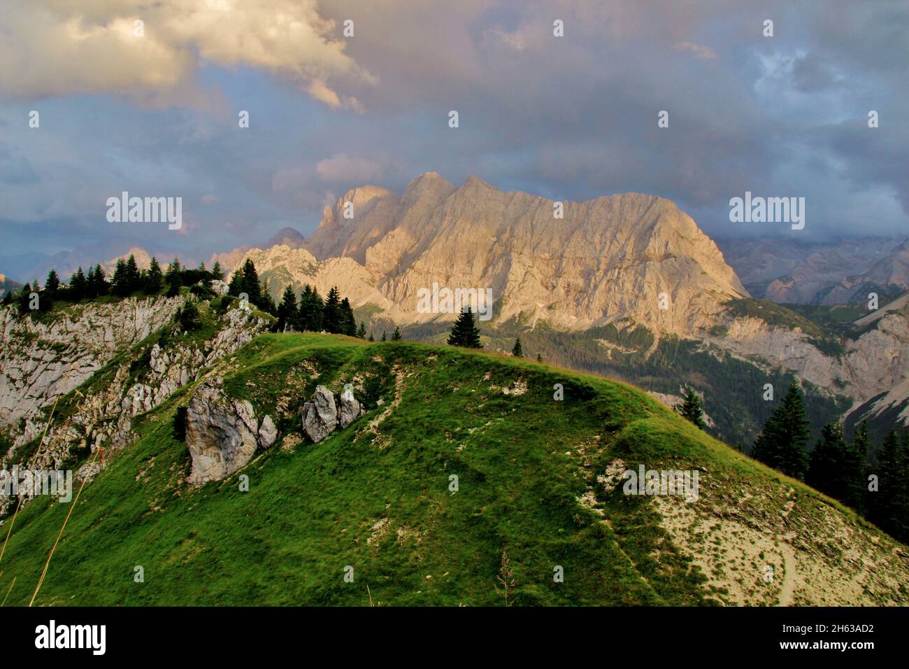 view to the eastern karwendelspitze (2537m),vogelkarspitze (2522m),hintere schlichtenkarspitze (2473m),bäralplekopf (2323m),evening hike to the soiernspitze (2257m),sunset,grassy mountain edge on the jöcherle in the foreground,dramatic cloud mood,karwendel mountains,mittenwald,upper bavaria,bavaria,werdenfels,germany,europe Stock Photo