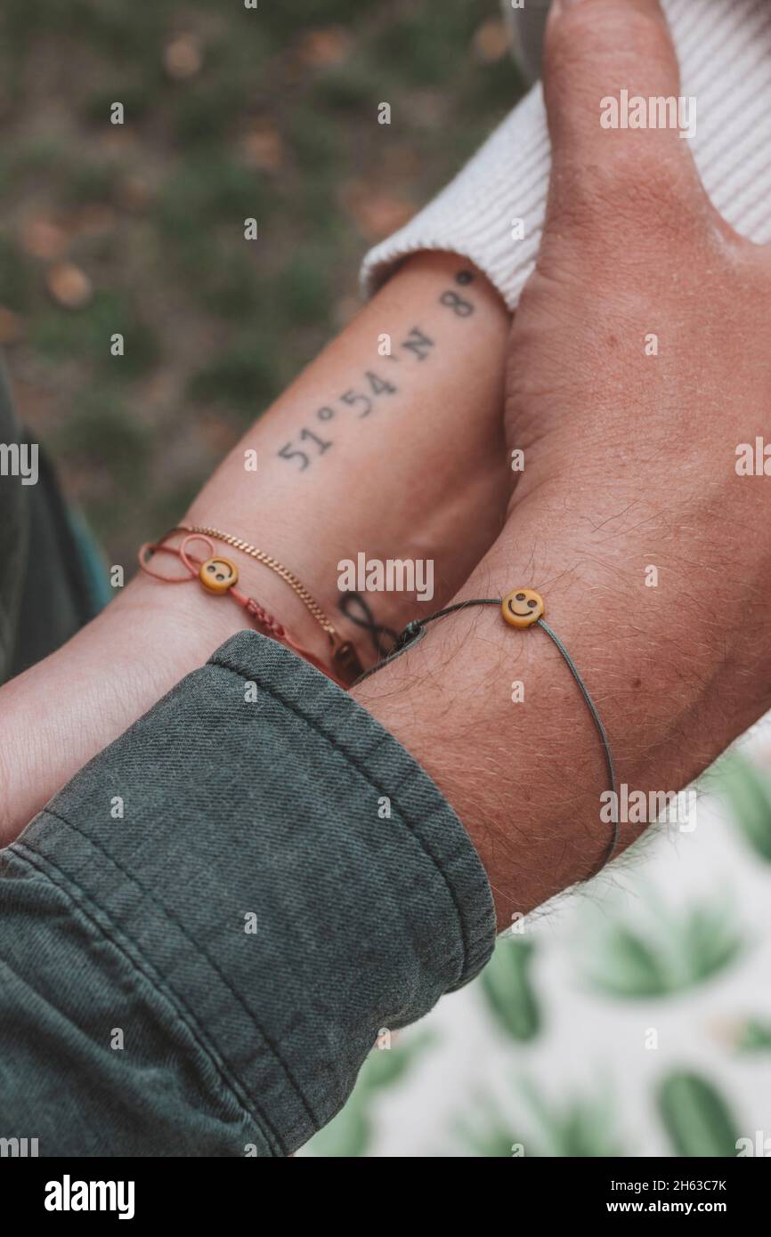 young couple at engagement shoot,holding hands,friendship bracelet with emoji face,coordinates tattoo Stock Photo