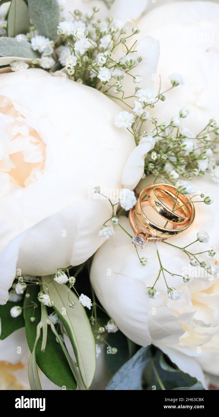 bridal bouquet close-up in white with peonies and gypsophila,wedding rings and engagement ring in focus Stock Photo