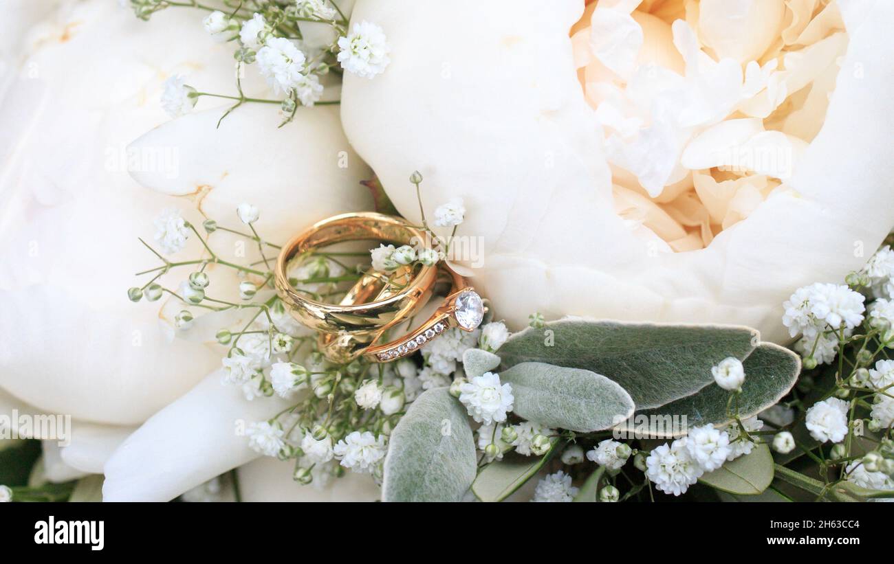 bridal bouquet close-up in white with peonies and gypsophila,wedding rings and engagement ring in focus Stock Photo