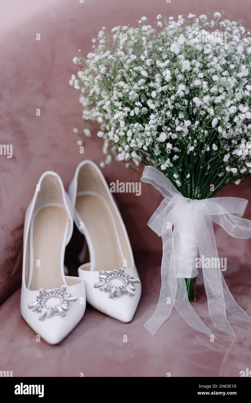 Composition of a beautiful white wedding bouquet with a pair of fashionable wedding shoes on a pink background Stock Photo