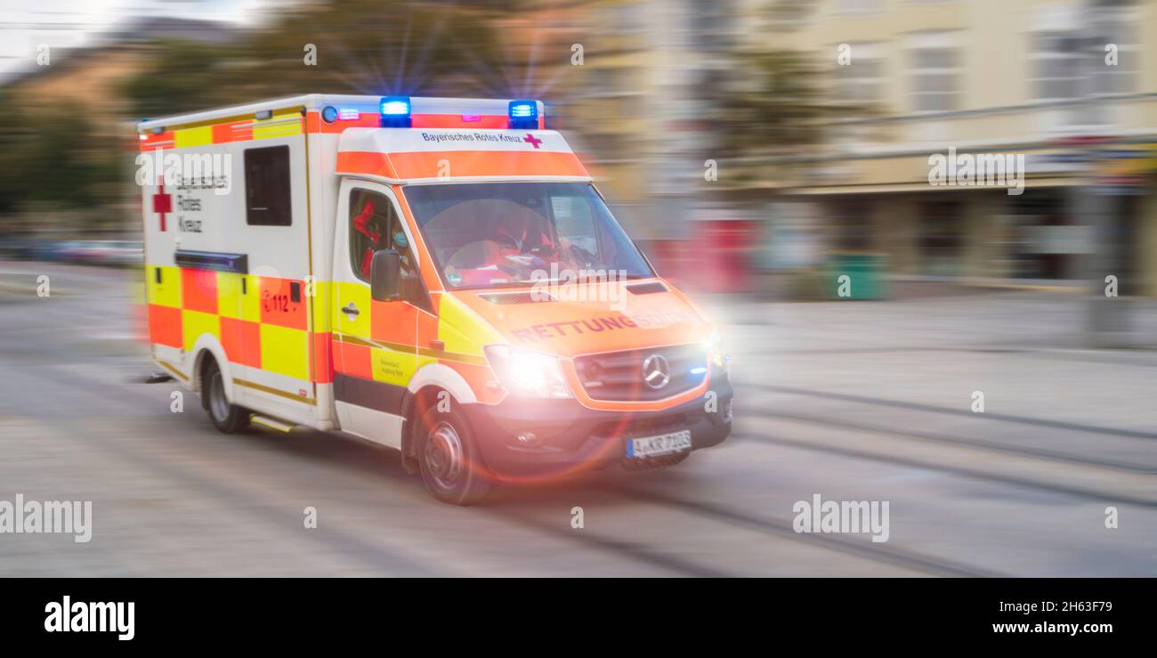 an ambulance from the red cross drives through augsburg with flashing lights and high speed Stock Photo