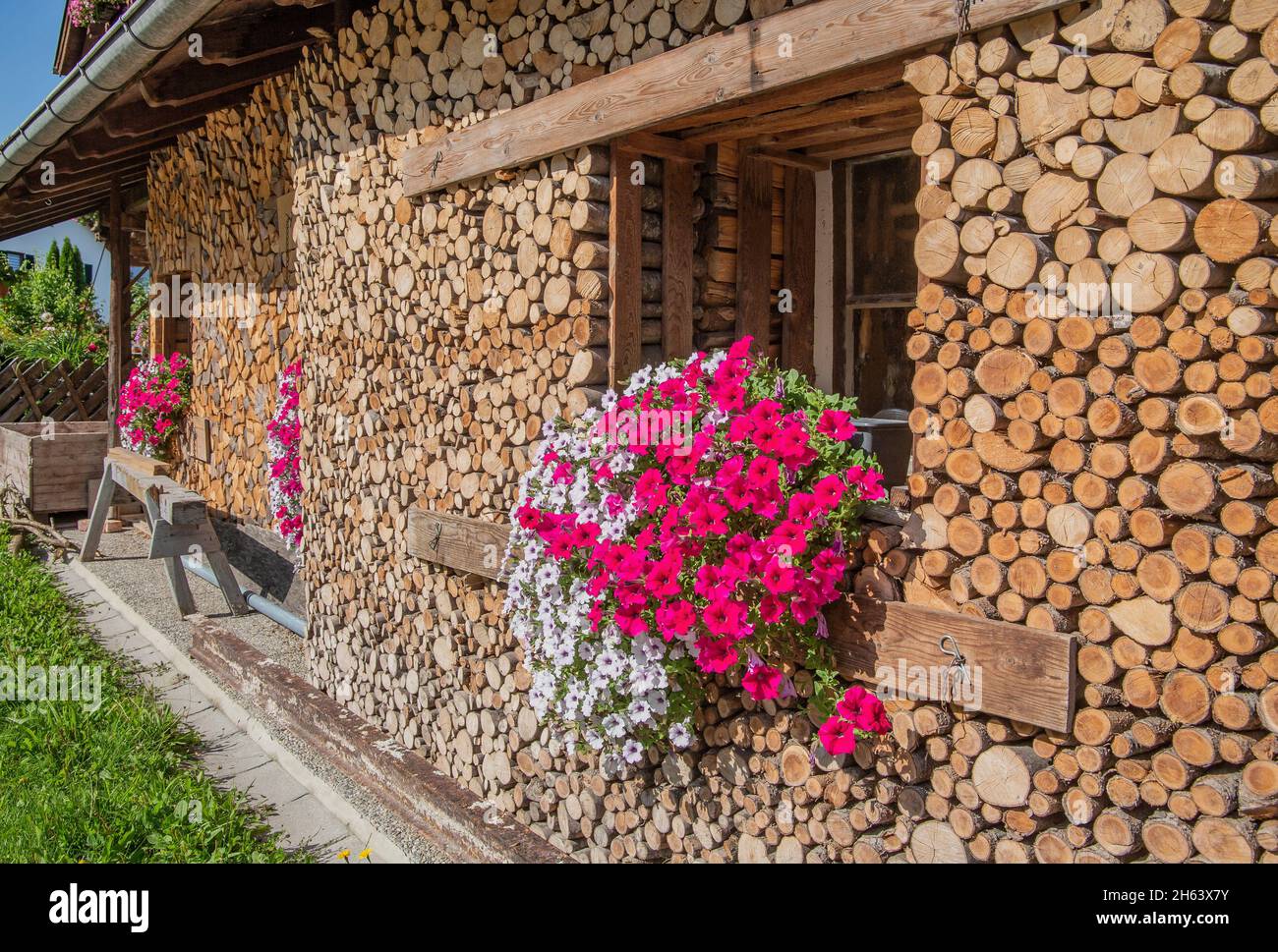 window with flower box on house wall with stacked firewood,ohlstadt,loisachtal,das blaue land,upper bavaria,bavaria,germany Stock Photo