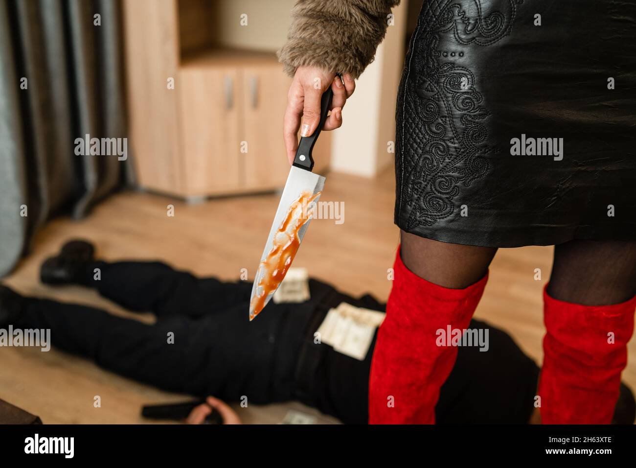 Close up on midsection of unknown woman female murderer holding bloody knife with unknown man lying dead on the floor stabbed with money banknotes aro Stock Photo