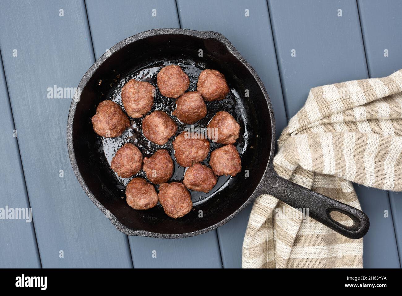 Homemade beef meatballs fried in cast iron pan with flax cloth on gray