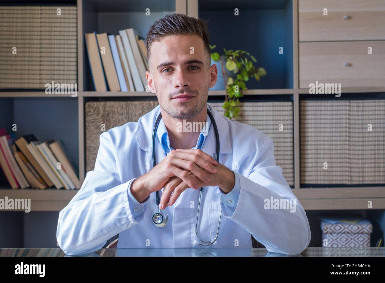 headshot portrait of smiling young male gp or physician in white medical uniform and glasses look at camera posing in hospital,happy caucasian man doctor show confidence skills in clinic workplace Stock Photo