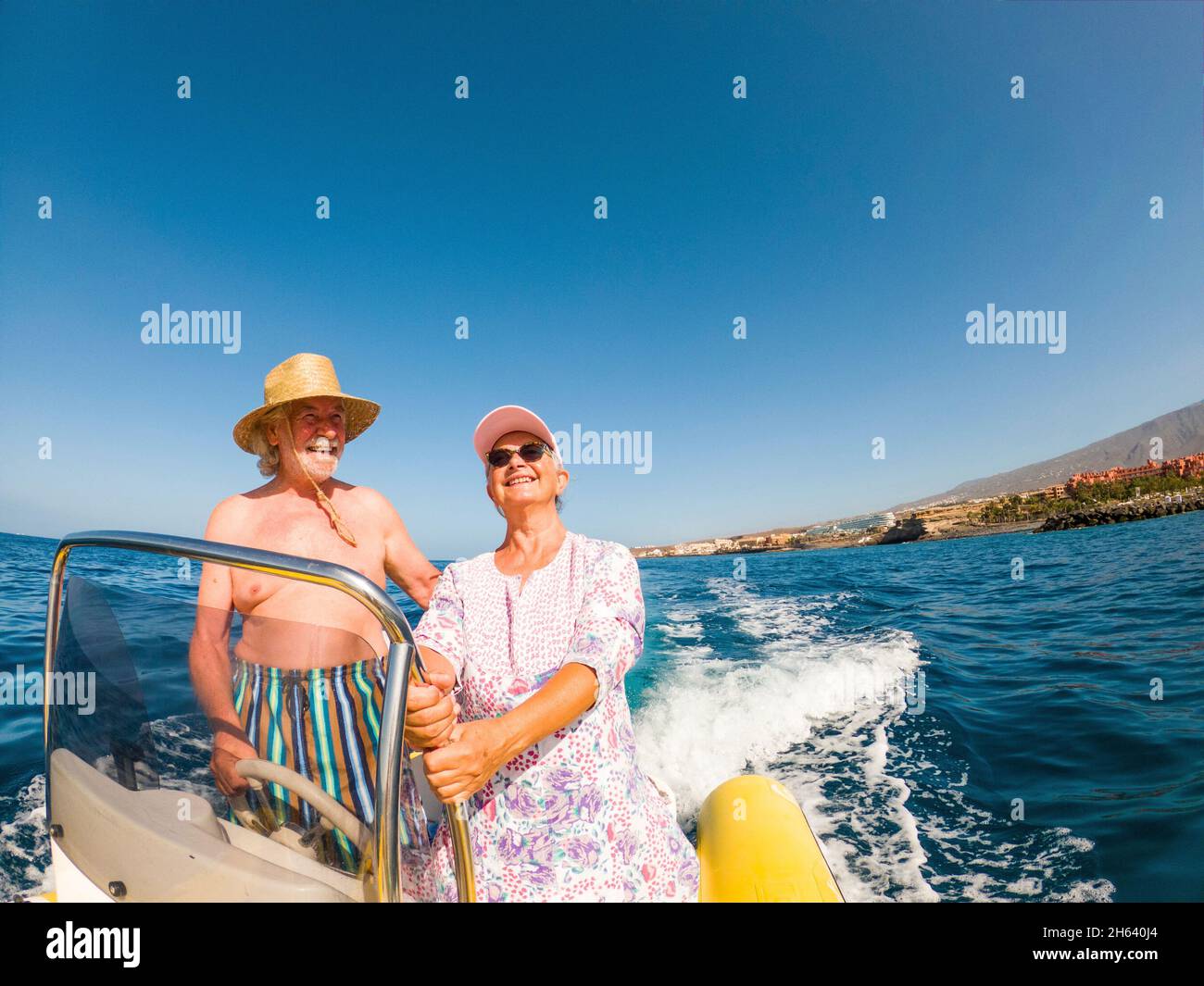 beautiful and cute couple of seniors or old people in the middle of the sea driving and discovering new places with small boat. mature woman holding a phone and taking a selfie with hew husband Stock Photo