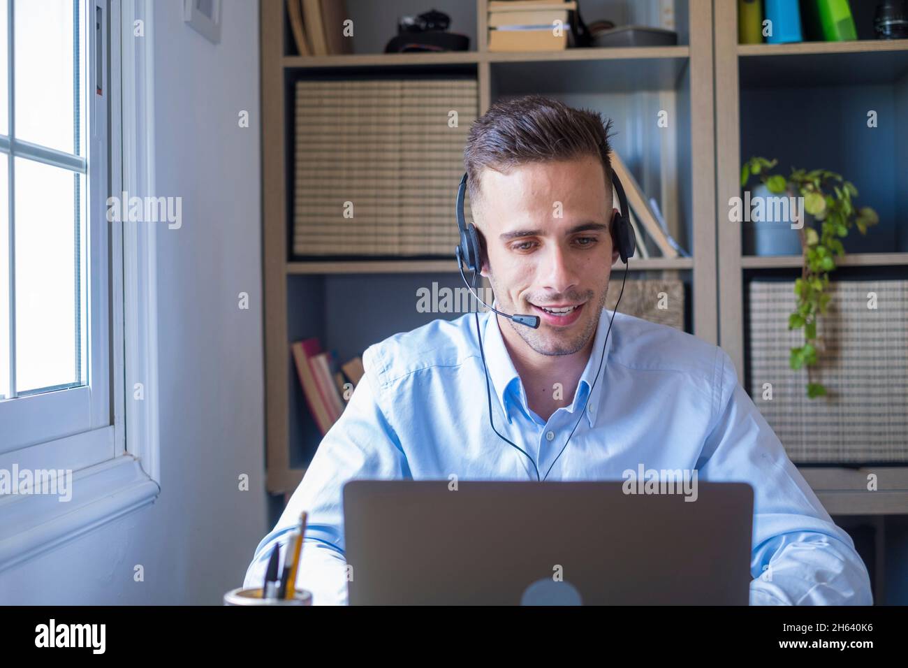 attractive caucasian man sit at homeoffice room wearing headset take part in educational webinar using laptop. video call event with clients or personal chat with friend remotely concept Stock Photo