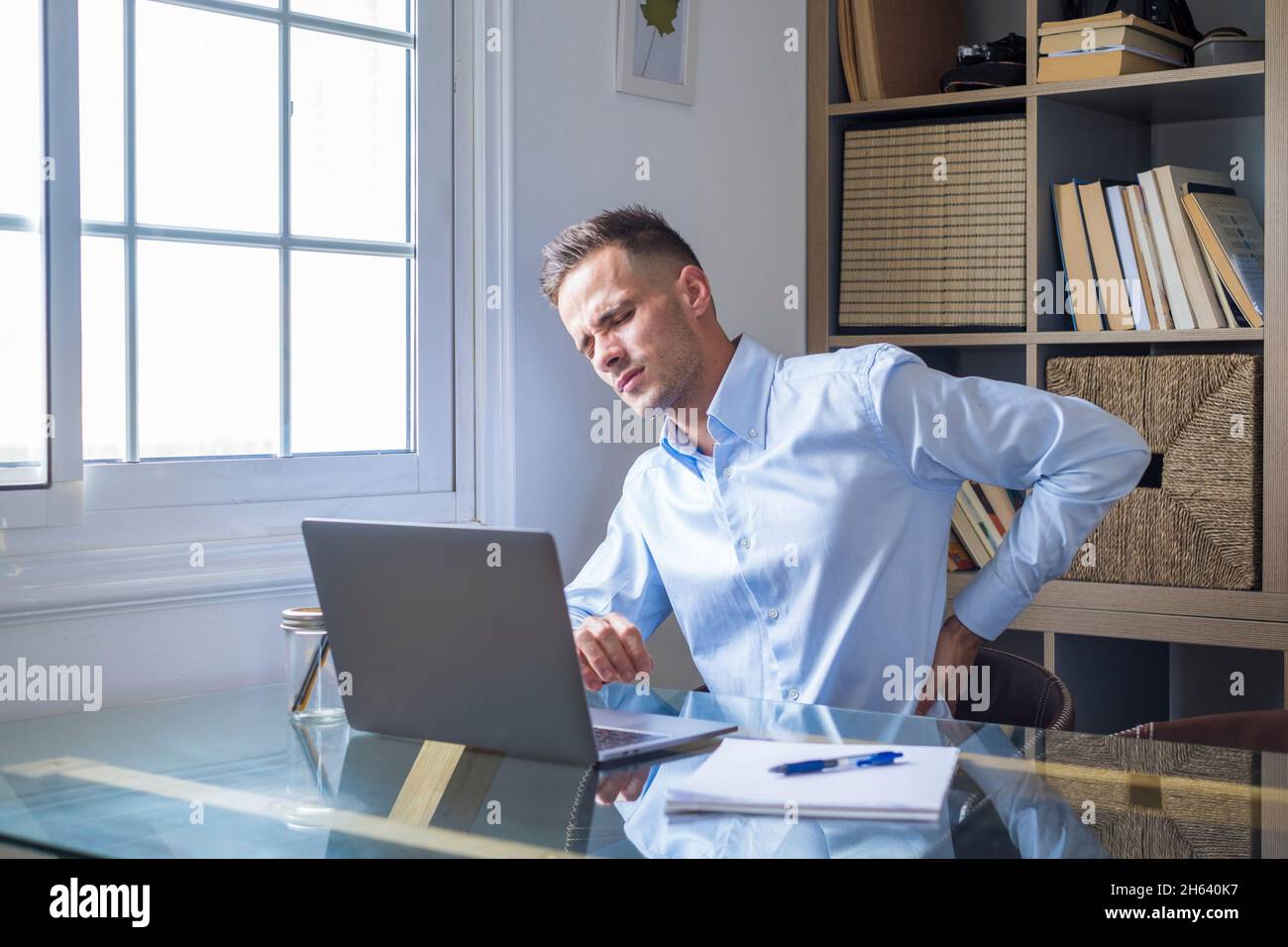 close up rear view stressed young man touching lower back feeling discomfort,suffering from sudden pain due to sedentary lifestyle or long computer overwork in incorrect posture at home office. Stock Photo
