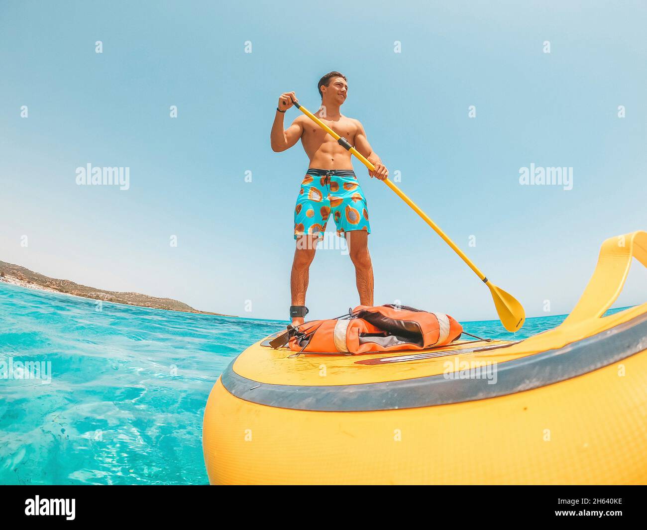 one happy caucasian man enjoying and having fun in vacations outdoors in the beach riding a paddle surf in the water. attractive boy feeling free traveling. Stock Photo