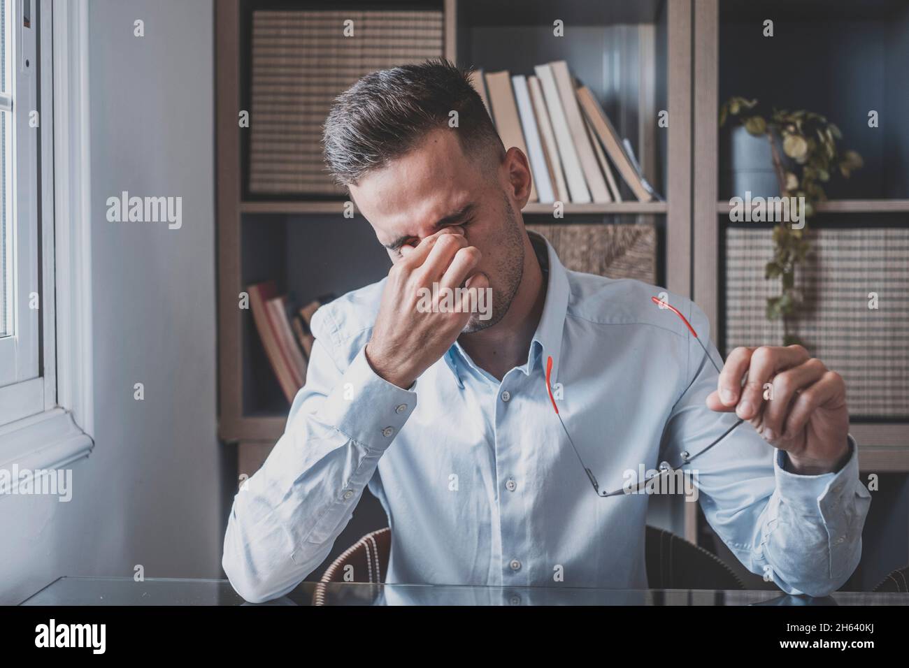 unhealthy stressed businessman taking off eyeglasses,rubbing eyelids,suffering from dry eyes syndrome due to long computer overwork,massaging head bridge relieving pain at office at home. Stock Photo