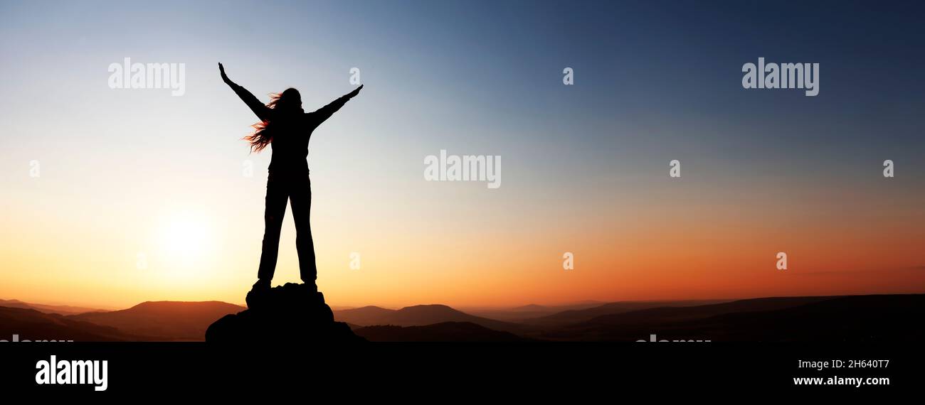 woman with arms raised over the horizon at sunset Stock Photo