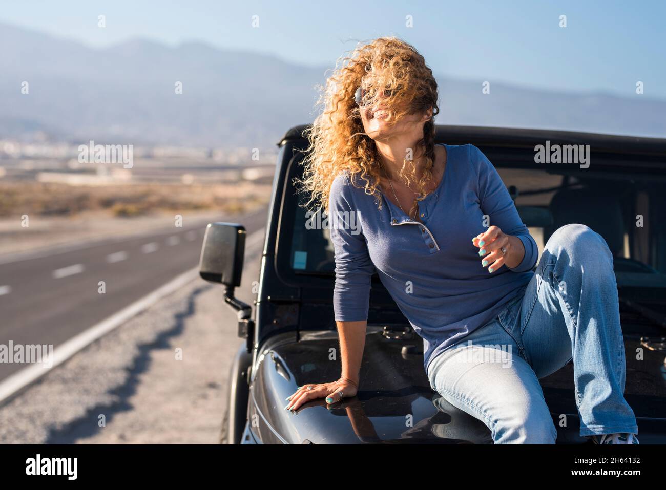 cheerful happy,lady sitting on the car in travel adventure vacation smile and enjoy freedom - driver and vehicle with road in background - concept of joyful single lifestyle people Stock Photo