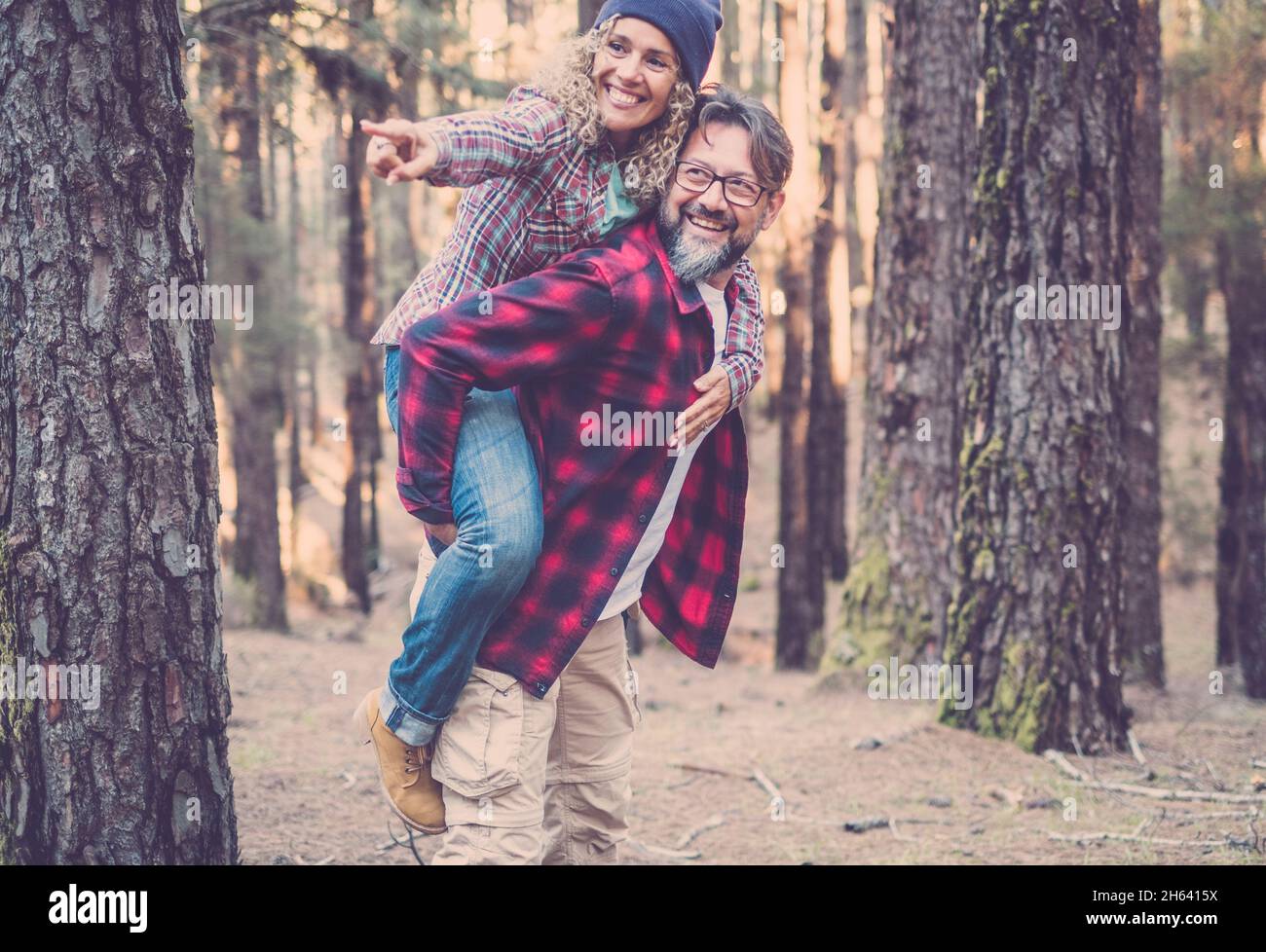 playful happy handsome caucasian couple having piggyback while walking on trail in woods. adventure in nature concept - young adult man and woman enjoy together outdoor leisure Stock Photo