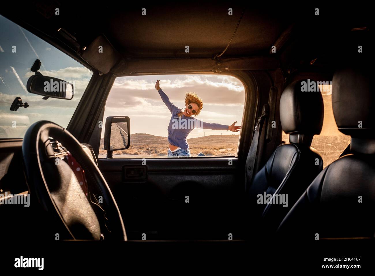 happy woman in travel adventure lifestyle summer vacation jump with hoyful and smile outside the car viewed from inside through the door - concept of road trip and female driver - freedom journey life Stock Photo