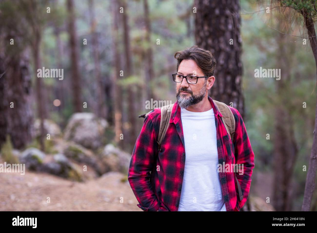 portrait of handsome young adult man walking in the woods alone enjoying outdoor leisure activity alone in natural forest - concept of adventure and trekking active people - travel lifestyle hipster male Stock Photo