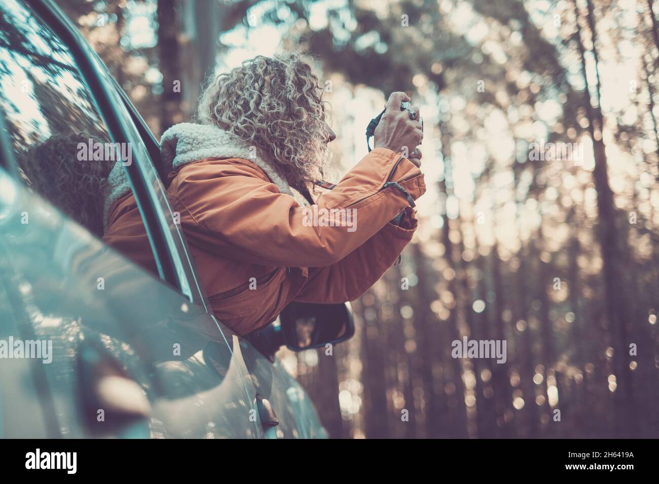 adventure vacation,holidays,travel,road trip and people concept - happy smiling young adult woman or young woman outside the car window taking picture to the forest woods nature Stock Photo