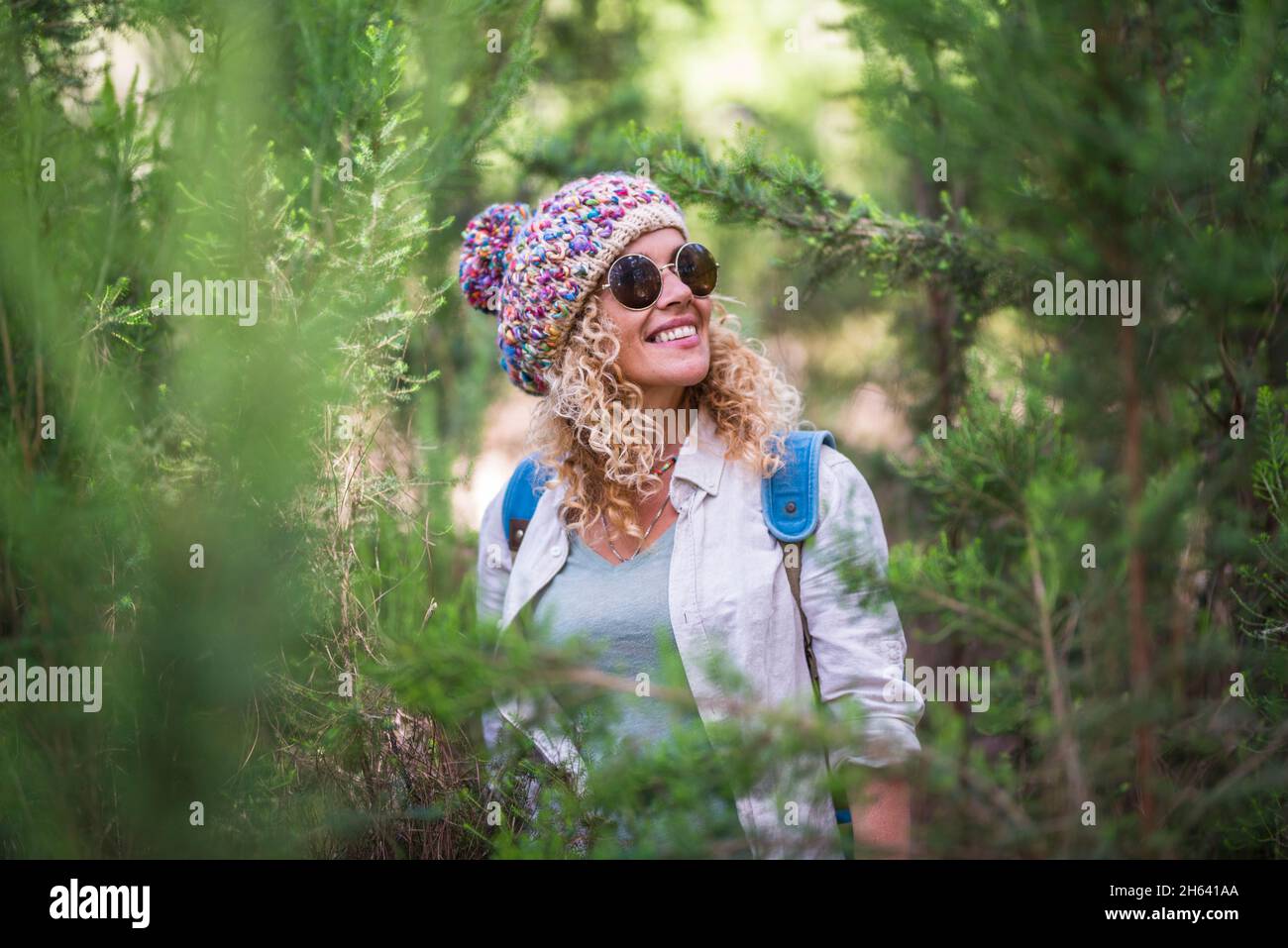 pretty adult cheerful woman smile and enjoy the outdoor nature forest leisure activity walking in the trees and green plants with a backpack - beautiful female people portrait outside enjoying adventure vacation Stock Photo