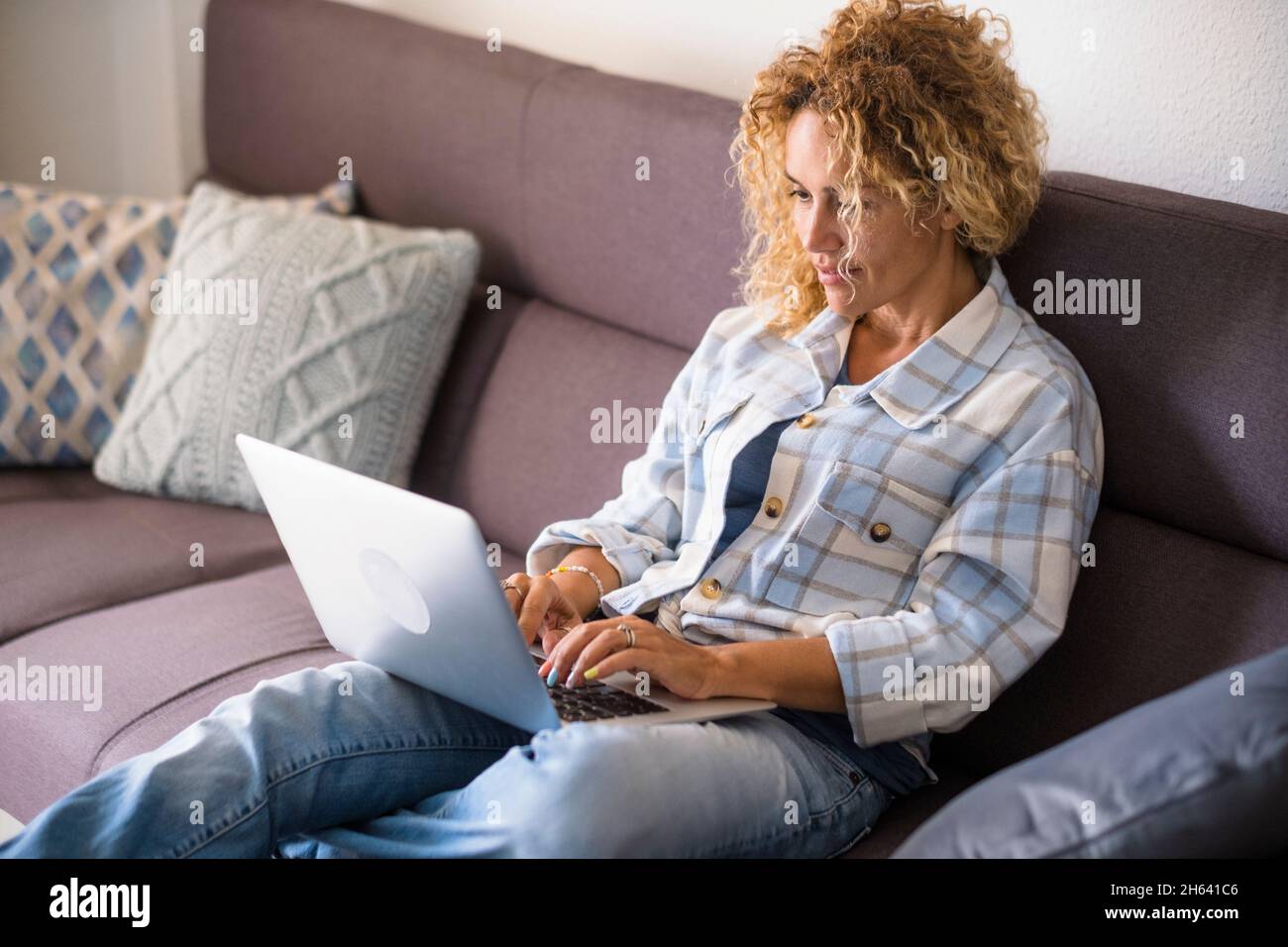 adult pretty female people watch internet computer contents lay down and relaxing on the couch at home - woman smile looking display and enjoy alternative job and work lifestyle - lady with glasses Stock Photo