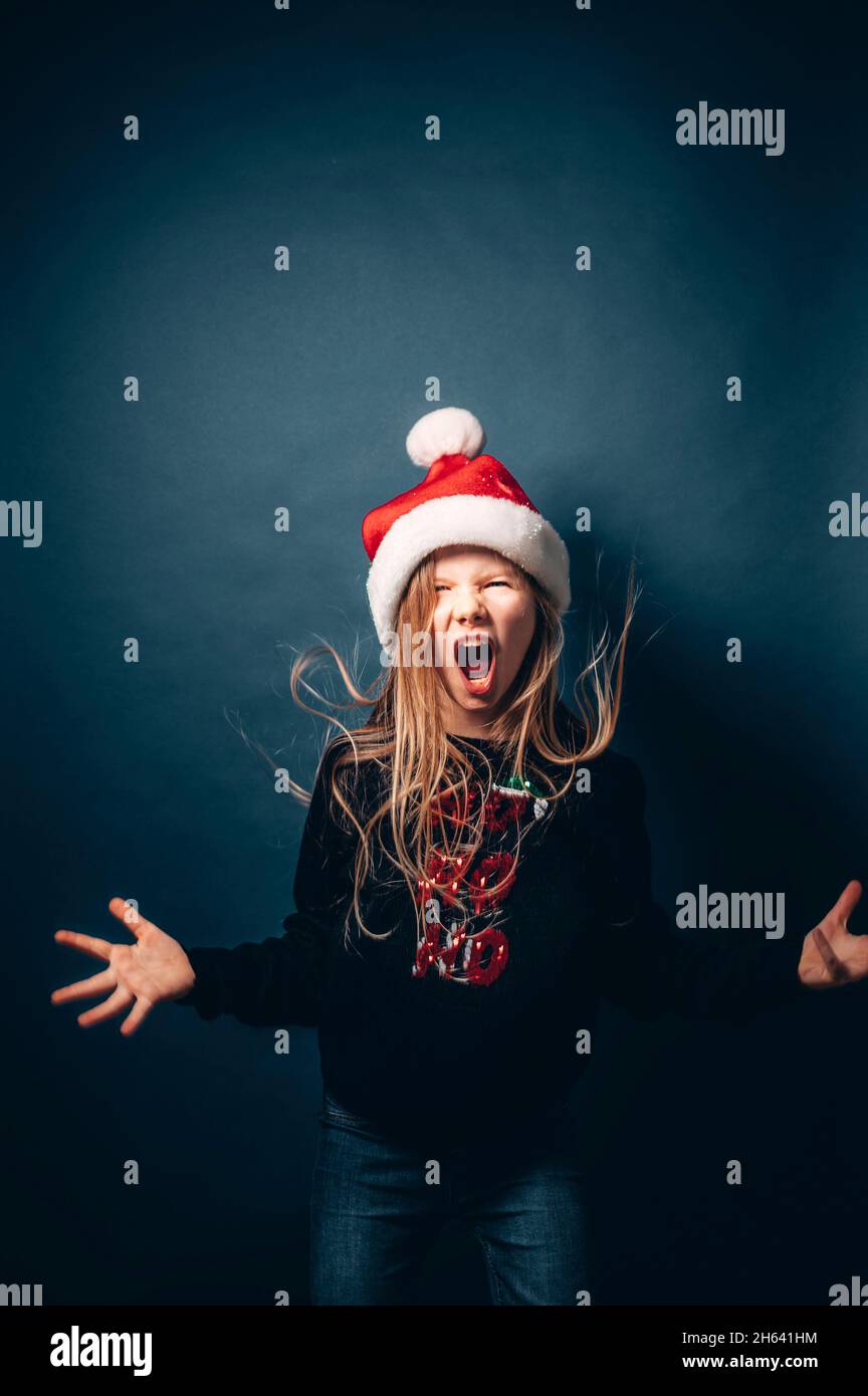 studio shot of a child wearing a christmas hat and pullover making fun in front of a blue background Stock Photo