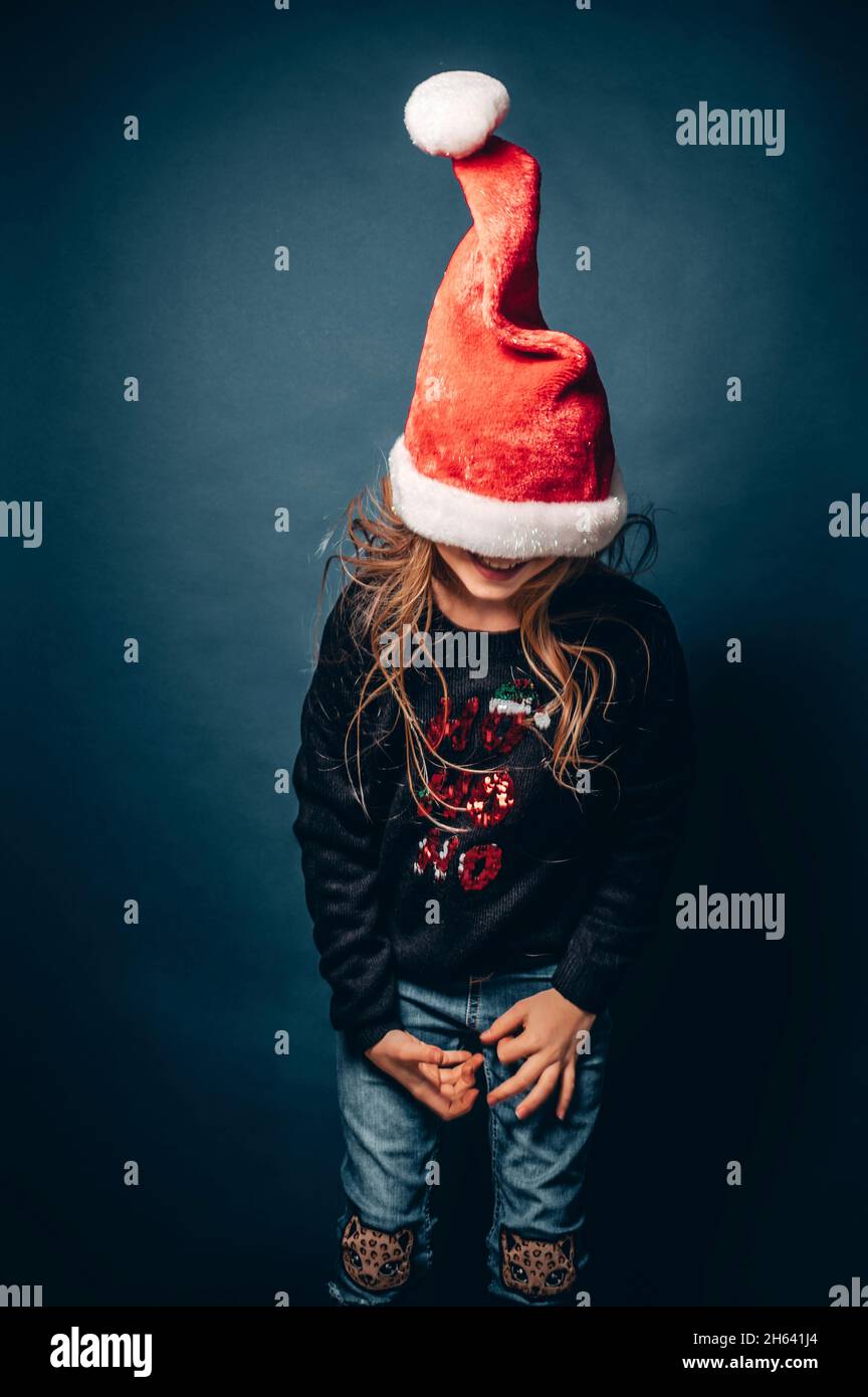 studio shot of a child wearing a christmas hat and pullover making fun in front of a blue background Stock Photo