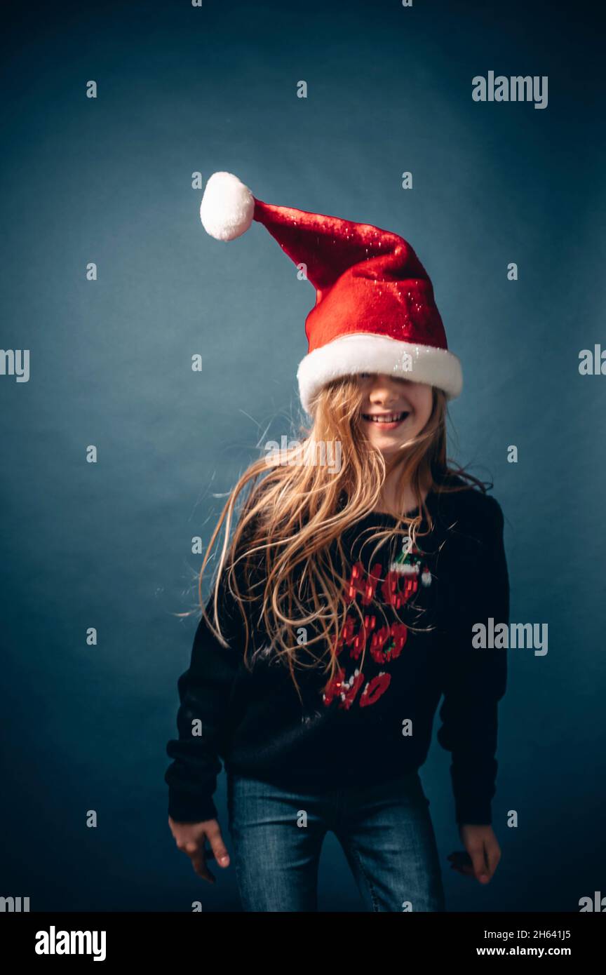 studio shot of a child wearing a christmas hat and pullover making fun in front of a blue background Stock Photo