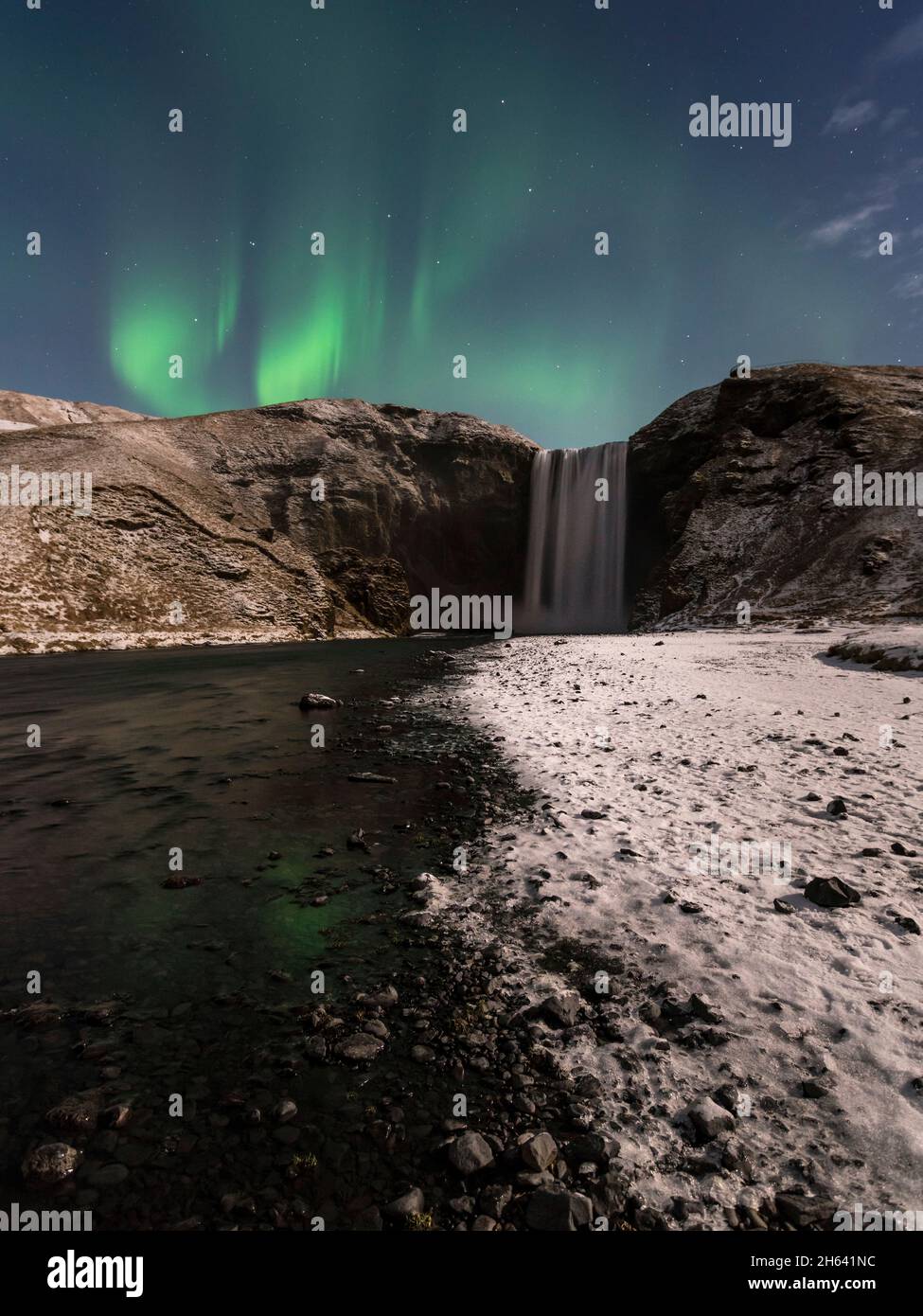 nocturnal northern lights on snowy skogafoss in iceland. Stock Photo