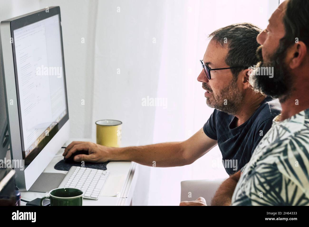 two employees working on desktop computers together. mature men working as a team while using desktop computer. two men busy working on computer,reading email on monitor screen Stock Photo