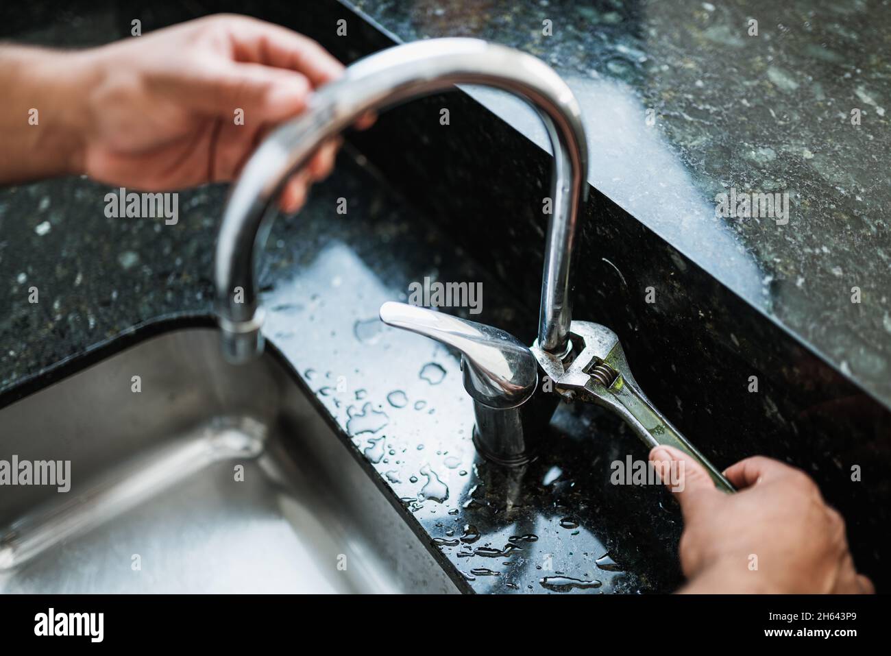 Close up of hands of aged repairman fixing broken kitchen tap using