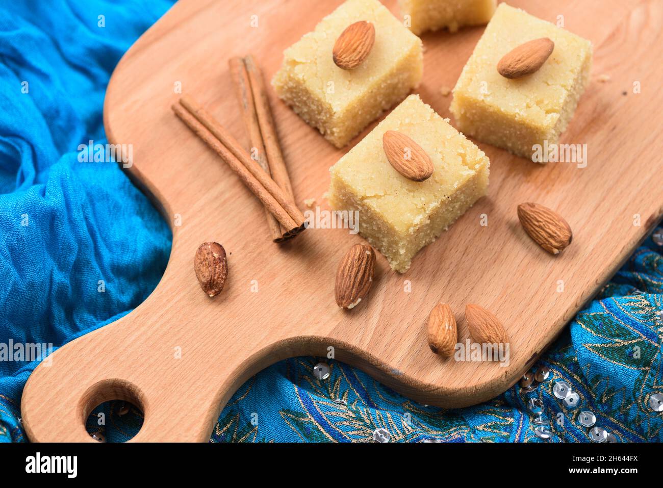 Halava, Indian sweetmeats cut in squares decorated with almonds on wooden board on indigo cloth top view Stock Photo