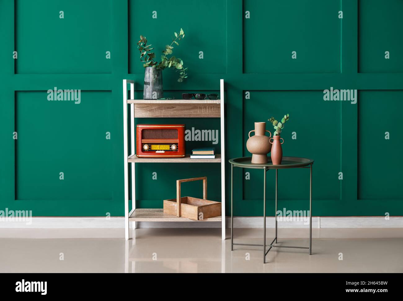 Bookcase with retro radio receiver and table near green wall Stock