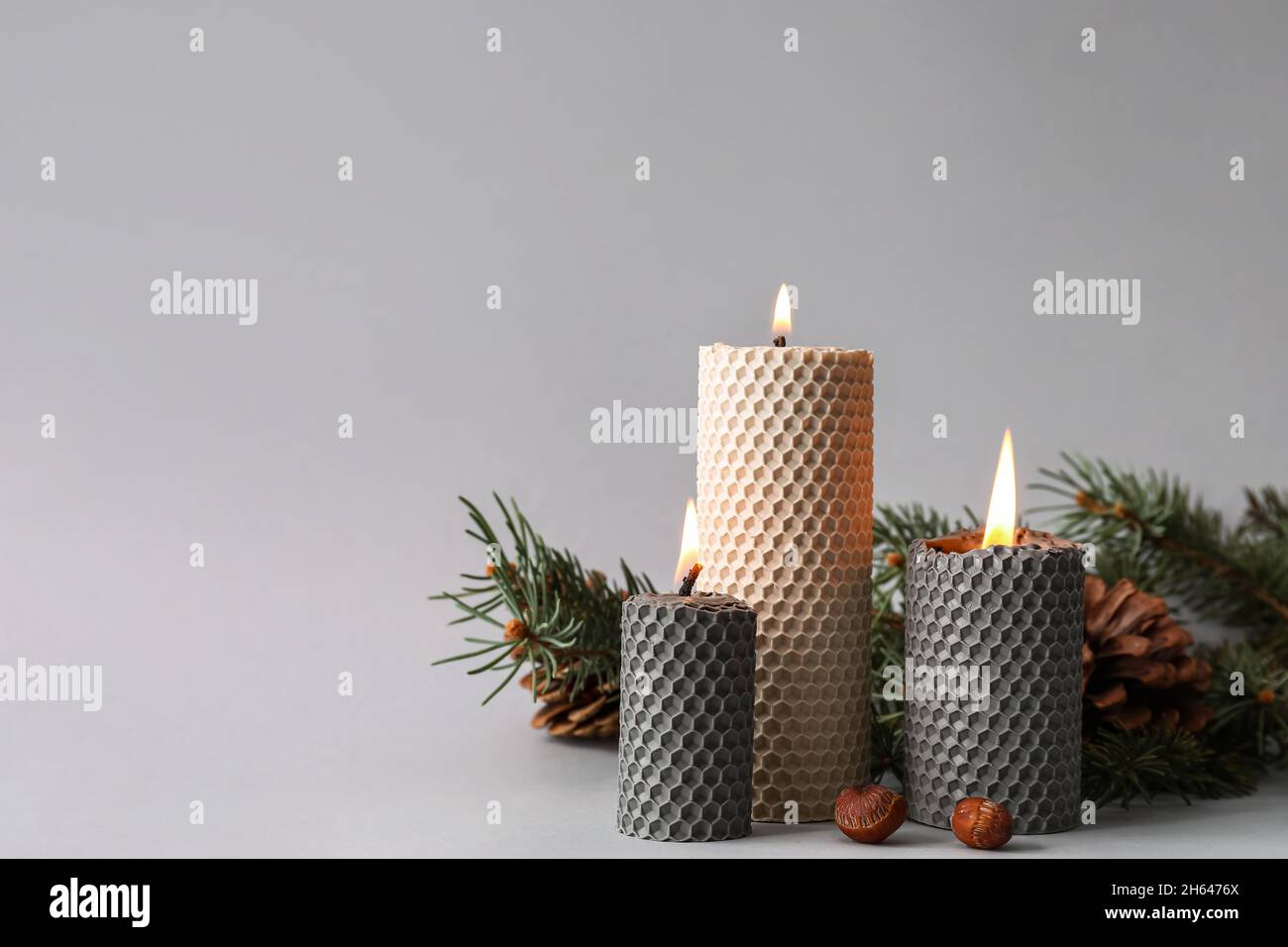 Burning candles, fir tree branches, pine cones and hazelnuts on grey ...