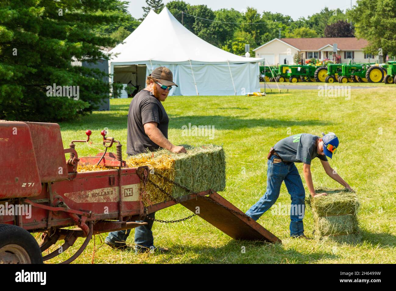 Two young farmers demonstrate the use of an antique New Holland model 271 hay baler at a tractor show in Warren, Indiana, USA. Stock Photo
