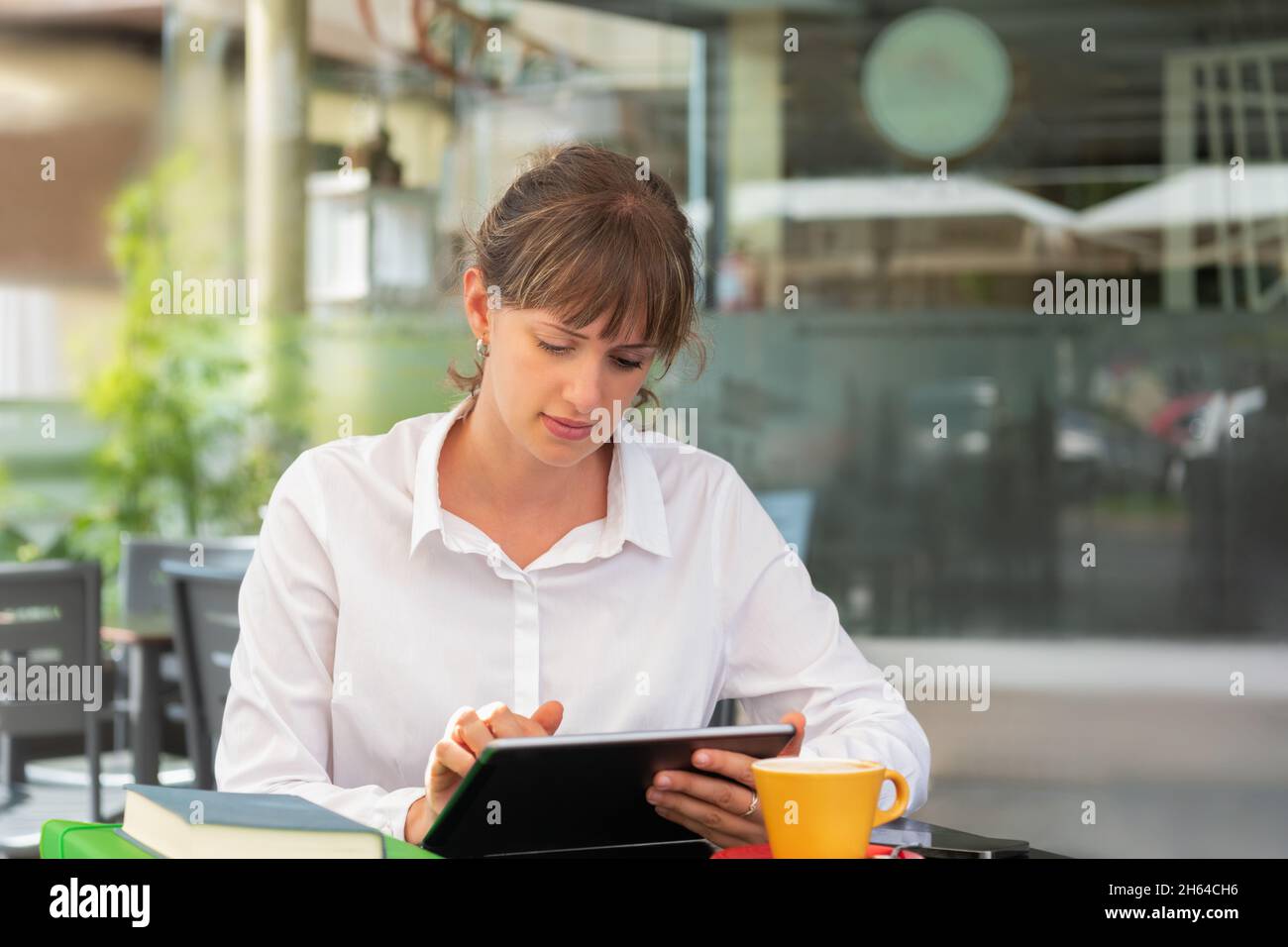 A businesswoman using her digital tablet in a cafe with a cup of coffee and some books and folders on the table Stock Photo