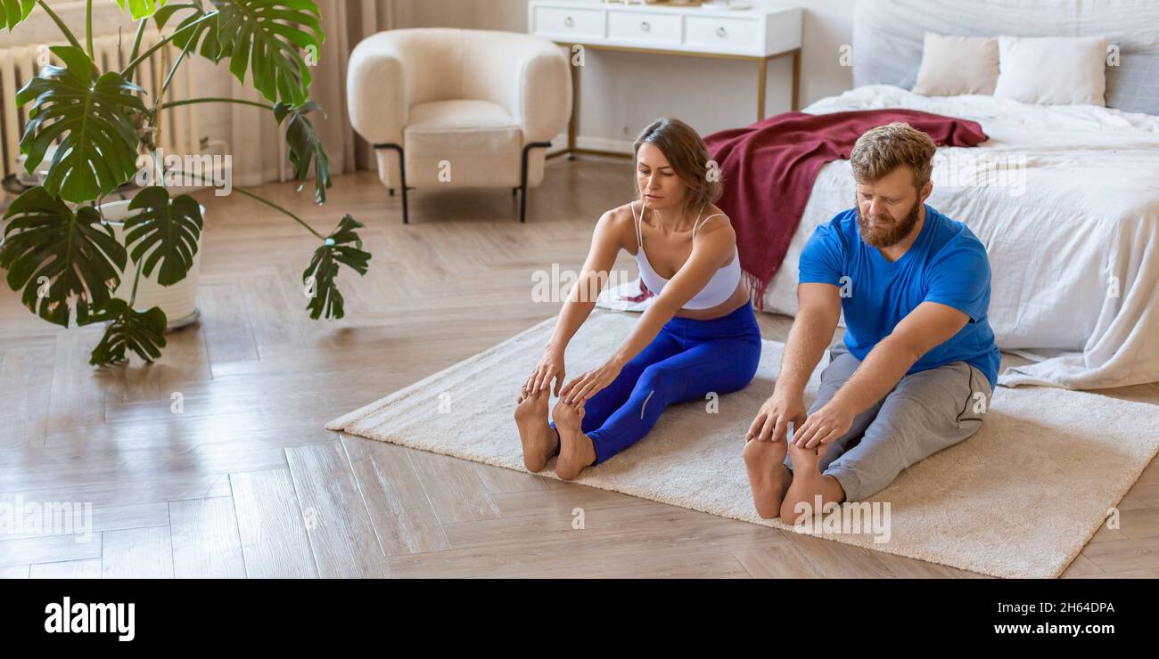 A middle-aged couple doing stretching together at home. The concept of a healthy lifestyle and maintaining oneself in shape after the age of 40. Forma Stock Photo