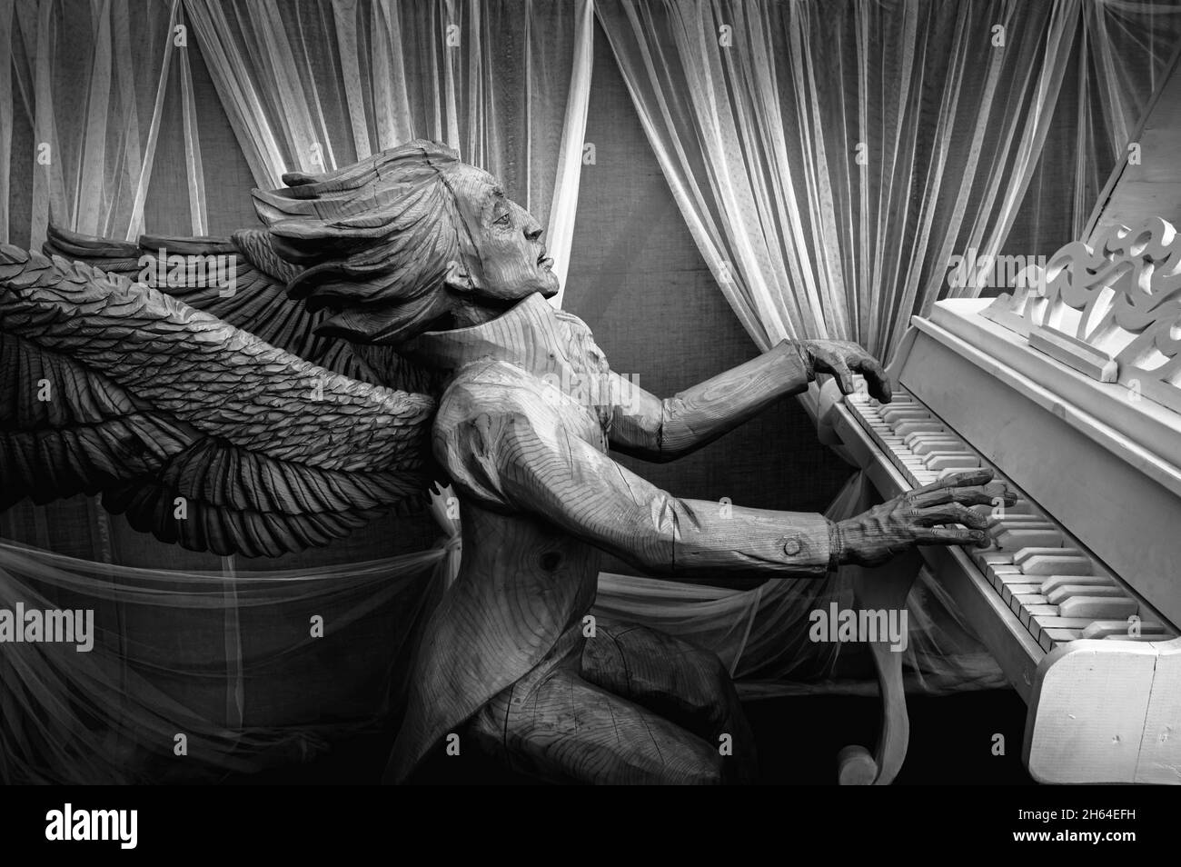 Wooden sculpture of an angel playing the piano in Ruskeala Mountain Park. Karelia, Russia. Black and white. Stock Photo