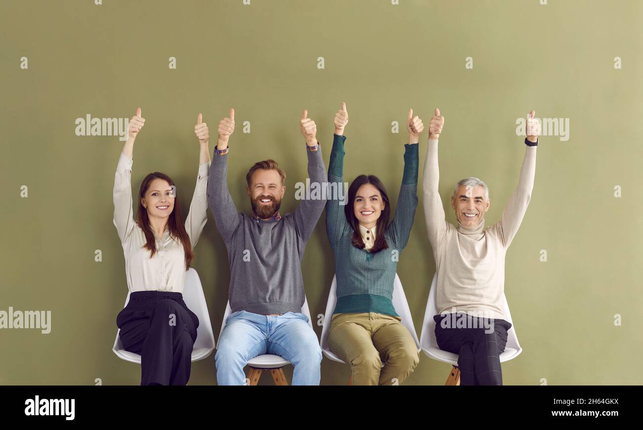 Portrait of four happy satisfied people sitting in row with arms raised and showing thumbs up. Stock Photo