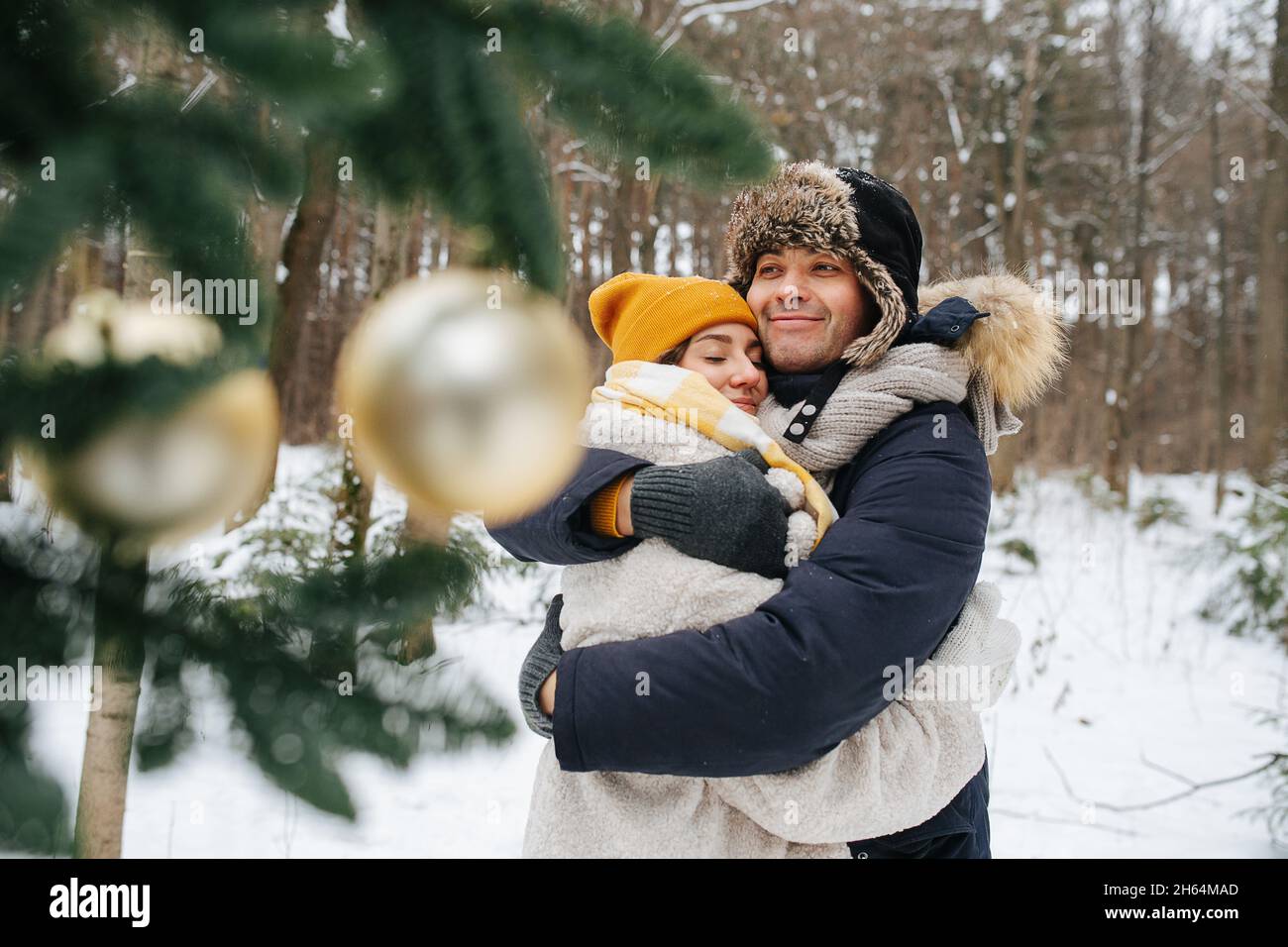 Loving couple in winter, hug standing behind a decorated Christmas tree.  Stock Photo