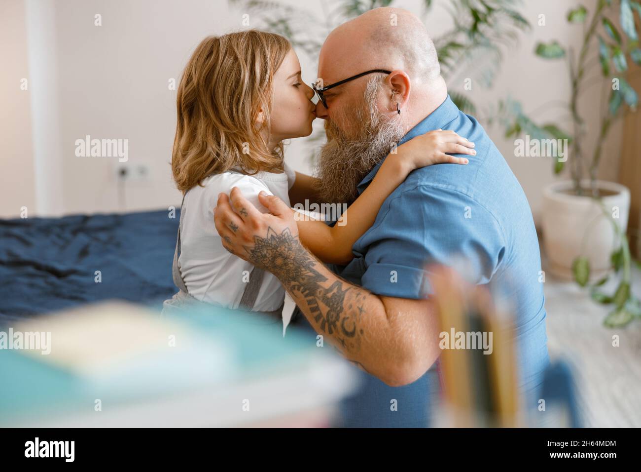 Short haired little girl hugs and kisses happy father nose sitting on bed at home Stock Photo