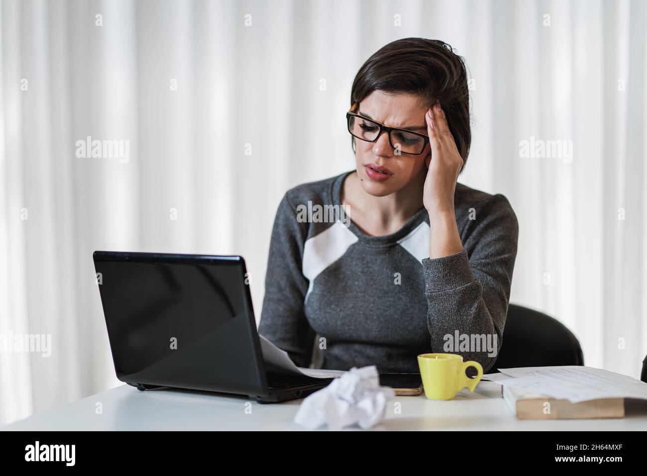Stressed Latin woman suffering migraine with a laptop sitting in a ...