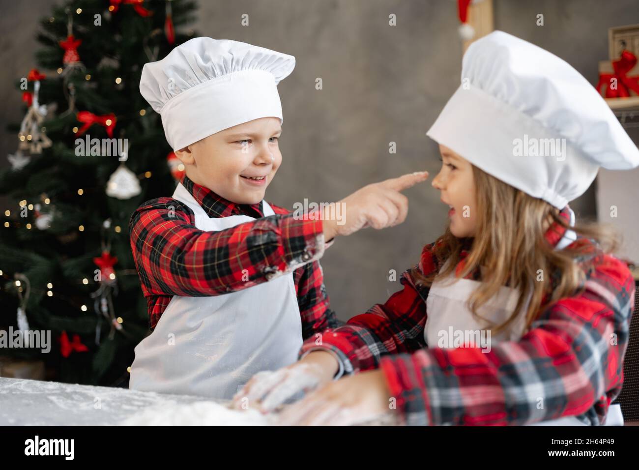 Christmas baking. Cute kids brother and sister play and get dirty with flour in the kitchen. Children make Christmas gingerbread cookies Stock Photo