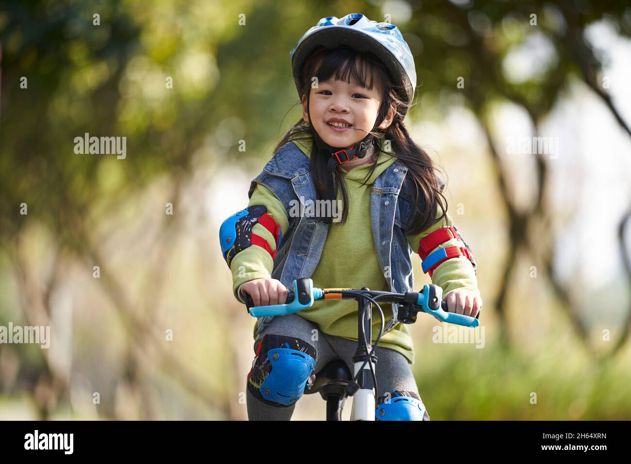 lovely happy asian little girl with helmet and full protection gear riding bike in city park Stock Photo