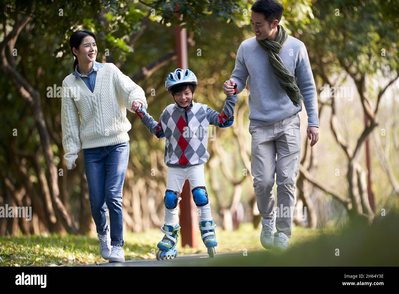 loving asian parents teaching son roller skating outdoors in city park Stock Photo