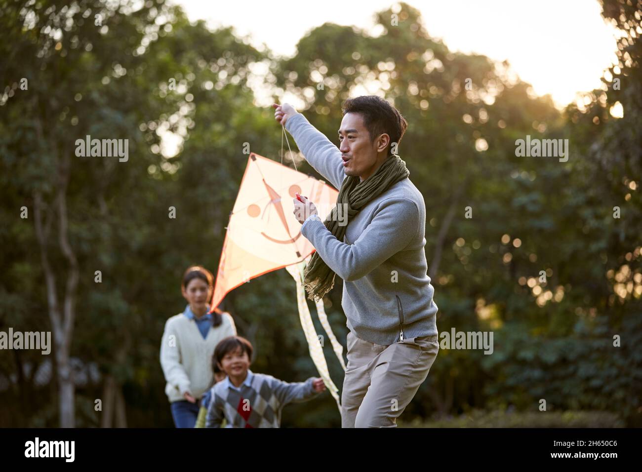 happy asian family flying a kite outdoors in city park Stock Photo