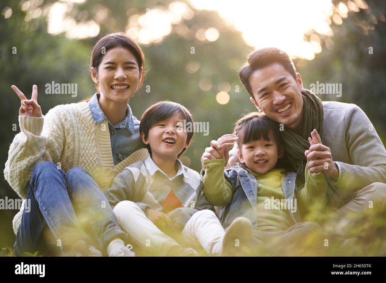 happy asian family with two children having good time sitting on grass in city park Stock Photo
